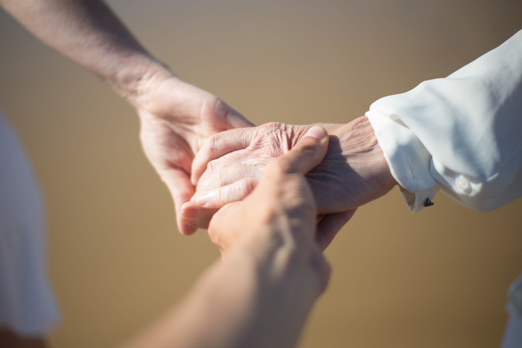 An older person's hand held gently between both hands of a home health professional